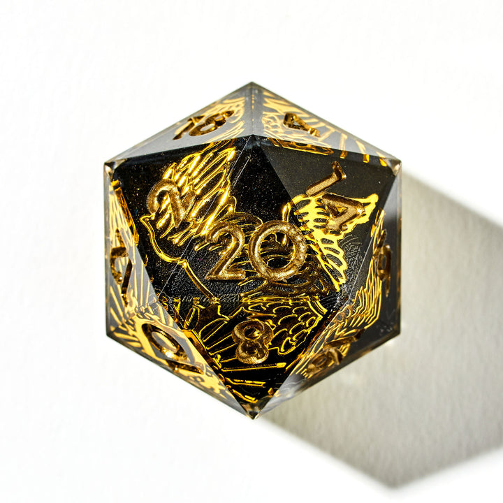 Close up of a black and gold D20 die with wing and sun designs